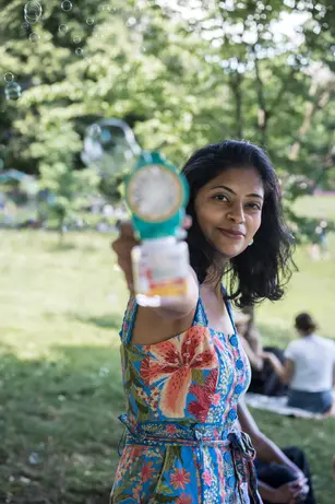 A woman aims a bubble gun toward the camera, the camera, with the hint of a smile.